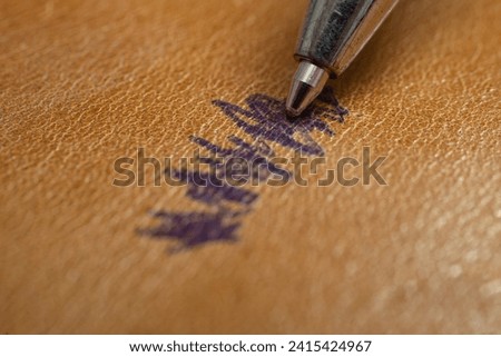 Ballpoint pen tip, scribbling on a brown leather sofa, or car seats, soft focus close up Royalty-Free Stock Photo #2415424967