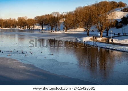 Walkers on the half-frozen lake in a park in Munich, Germany in winter.  The lake is part of the canal system that was built in the 18th century to transport goods and people Royalty-Free Stock Photo #2415428581