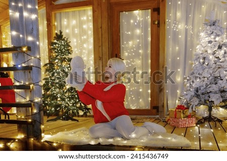 Woman by Christmas tree. Festive setting. Illustrating holiday cheer and celebration. She is posing for a picture, and there are presents nearby, adding to the festive atmosphere.