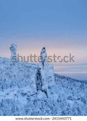Rock pillars, weathering posts. High stone cliff covered with snow and rise above the coniferous forest at sunset. Perm region, vertical view. 