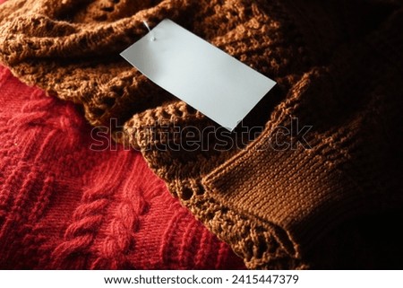 Texture of a knitted red sweaters in a cozy environnement. Warm atmosphere. There is a price tag hanging from one of the dresses.  Perfect background. E-commerce.