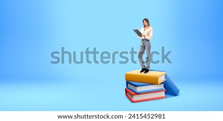 Smiling woman reading a paper document, standing on stack of cartoon books. Copy space empty blue background. Concept of education, student, knowledge and literature
