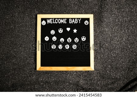 letter board ,wooden frame with the words welcome baby and a white smile emoticon decorated with flowers in the corner, top angle