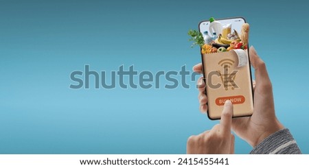 Online grocery shopping app: customer holding a smartphone and ordering groceries online Royalty-Free Stock Photo #2415455441