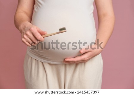 Pregnant woman holding a toothbrush, studio pink background. Concept of pregnancy and brushing teeth Royalty-Free Stock Photo #2415457397