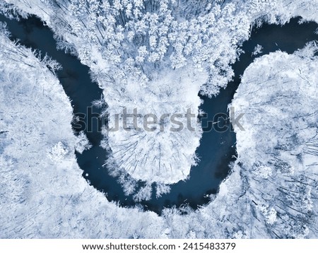 Top down view of river flowing in snow-covered forest in winter. The trees are covered with snow.