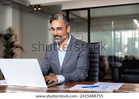Happy mature European business man ceo trader using computer, typing, working in modern office, doing online data market analysis, thinking planning tech strategy looking at laptop with copy space. Royalty-Free Stock Photo #2415488755