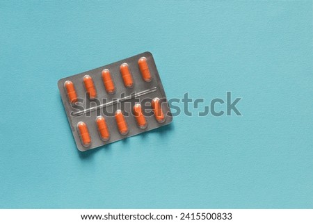 Blisters of tablets with orange capsules on a plain blue background. Pharmacy products. Medicine pills.	