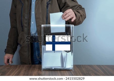 A voter casts a ballot into a ballot box on election day, Finland flag. Royalty-Free Stock Photo #2415502829