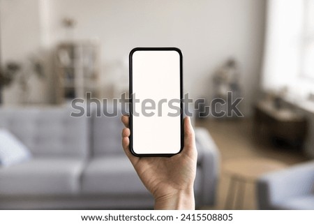 Close up shot of unknown female hand holding modern smartphone with white mock up blank screen, living room on background. Advertisement of new mobile application ad, smart home app, comfort living Royalty-Free Stock Photo #2415508805