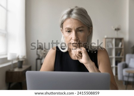 Close up of mature attractive thoughtful businesswoman learn new software, professional program, read received e-mail from client working online using laptop at home office room. Modern tech, business Royalty-Free Stock Photo #2415508859