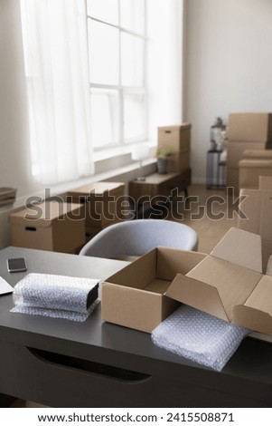 Vertical shot office with desk and heap of cardboard boxes stacked on floor. Workspace of small business owner, relocation day to new office, shipment, delivery, warehouse, individual entrepreneurship Royalty-Free Stock Photo #2415508871