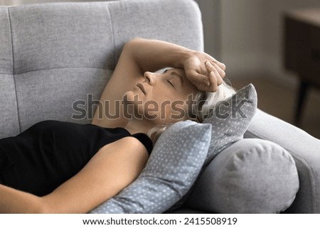 Close up calm mature female felt asleep lying down on couch at home, take break, having healthy daytime nap, restore strength and energy looks peaceful, relieving fatigue after hard working day. Rest Royalty-Free Stock Photo #2415508919