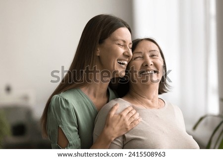 Joyful adult child woman hugging happy mom from behind, holding shoulders, talking, smiling, laughing, enjoying closeness, embracing mother with love, affection, care, gratitude Royalty-Free Stock Photo #2415508963