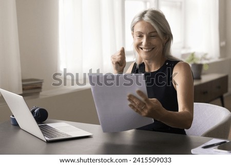 Happy attractive middle aged woman sit at table read postal letter correspondence, get good news in paper notice, make yes gesture, feels happy, receive loan approval, taxes refund, celebrate success Royalty-Free Stock Photo #2415509033