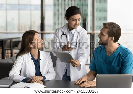 Beautiful young Indian doctor woman holding tablet, talking with colleagues, discussing diagnosis, giving consultation of expert. Multiethnic practitioners using gadgets for work discussion Royalty-Free Stock Photo #2415509267