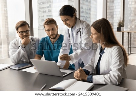 Young Indian medical team leader presenting job application on laptop to colleagues. Diverse doctors meeting at computer, talking on group video call, looking at screen, speaking, listening Royalty-Free Stock Photo #2415509401