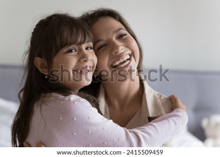 Close up of joyful little girl spend leisure time at home with loving mother, cute daughter hug caring young mom, smiling, look away, happy family express love and affection, enjoy strong family ties