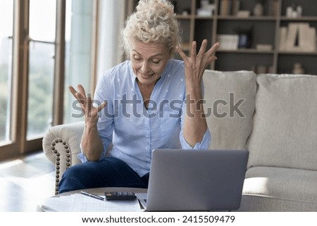Frustrated mature woman sit at table in living room, calculates expenses with calculator, feels annoyed unable to pay utility bills, worried, looks mad and nervous, anxious about debt or bankruptcy Royalty-Free Stock Photo #2415509479