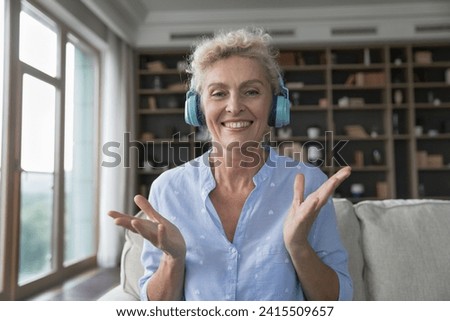 Head shot portrait happy middle-aged woman wear headphones smile, looking at camera, talking on video conference to family, webcam view. Virtual meeting, modern technologies usage for communication Royalty-Free Stock Photo #2415509657