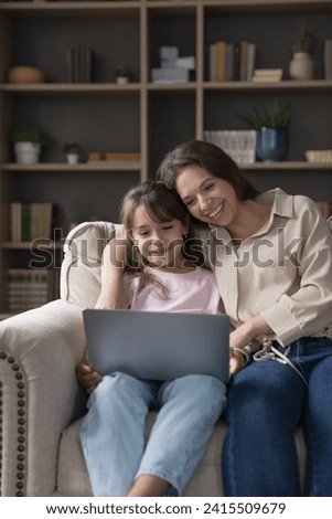 Vertical shot woman and cute little daughter spend weekend watching on-line cartoons, educational videos on laptop, enjoy pastime on internet, make order, purchasing trough electronic commerce website