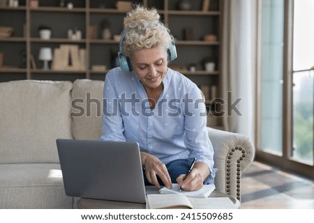 Smiling attractive middle-aged female in headphones listen audio course, improve foreign language knowledge, e-learning use laptop. Videocall to tutor, education, new skills gaining using modern tech Royalty-Free Stock Photo #2415509685