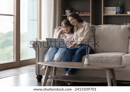 Family spend time at home using laptop, resting seated on comfortable sofa watch movie, on-line cartoons, educational program, enjoy new videogame for kids development. Modern tech usage, fun, leisure