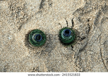 Exterior top view photo of two empty green glass bottle of beer on the sand of a beach making dirty pollution for the sea or ocean 
