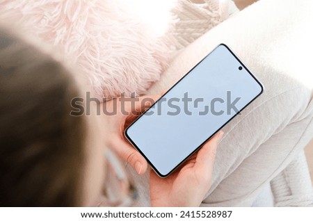 Woman using smartphone blank screen, cozy, modern design. Girl sitting on the chair in home interior. View from above.