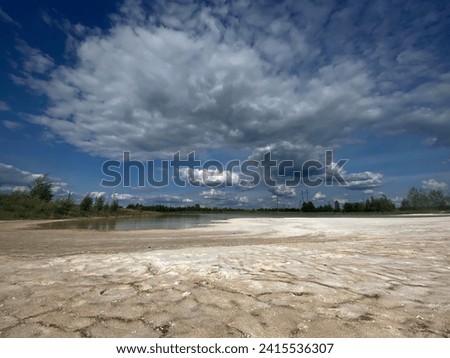 A dried-up lake with cracked parched earth due to drought in summer Royalty-Free Stock Photo #2415536307