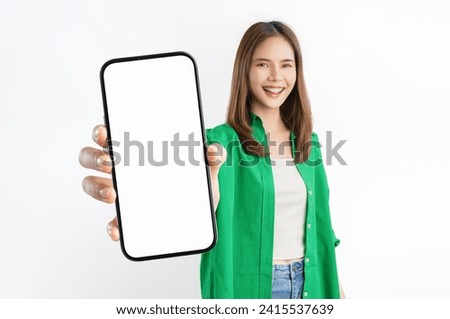 Cheerful beautiful Asian woman wearing green shirt and holding smartphone mockup of blank screen on white background.