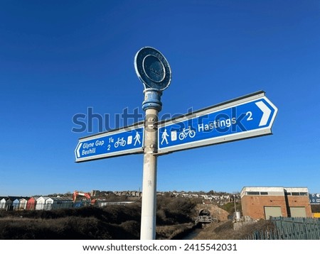 A sign indicates the cycle route and walkway section of a coastal path from Glyne Gap, Bexhill to Hastings.Mileages are shown. Blue sign against and sunny blue sky Royalty-Free Stock Photo #2415542031