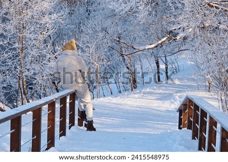 Girl sitting on wooden bridge in winter forest, frost and snow covered trees. Nature after snowfall, cold weather
