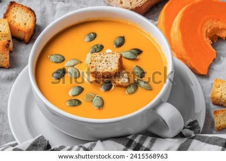 Composition with pot of tasty pumpkin cream soup and autumn leaves on wooden background