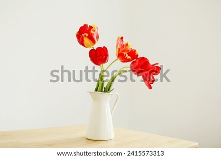 Bouquet of red flowers in a vase. Tulips on the table in a light  room. Cozy interior. Minimalism. Selective focus
