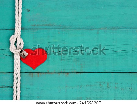 Silver lock and red wood heart hanging on knot of white rope border against blank antique teal blue weathered wooden background