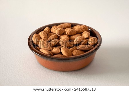 Almonds in a baked clay plate on white background Royalty-Free Stock Photo #2415587513