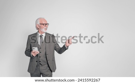 Smiling old male professional using smart phone and pointing at copy space over white background