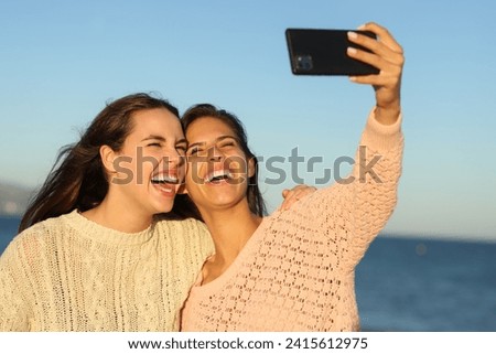 Two happy friends taking selfies laughing on the beach at sunset