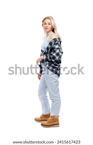Serious teenage girl standing. Cute blonde girl in jeans, plaid shirt and yellow shoes. Full height. Isolated on a white background. Vertical.
