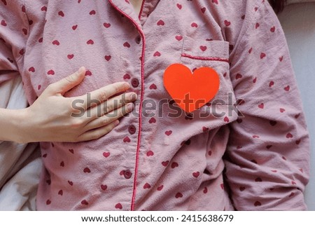 person in pajamas is lying in bed with red heart shaped postcard. surprise gift for Valentine's day, February holidays and vacations, tradition of declaring love giving gifts. Man woman relationship