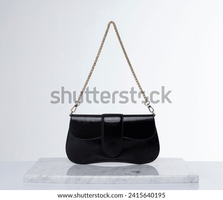 Black, shiny leather bag with gold chain, on a marble floor and white background in the studio