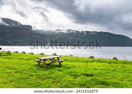 Table with picnic benches by the lake next the road to Roldal.  Picturesque landscape in Western Norway. Summer cold and rainy day. Scenic landscape in Western Norway. 
