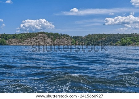 A blue and turbulent body of water is pictured with white, fluffy clouds in the sky above