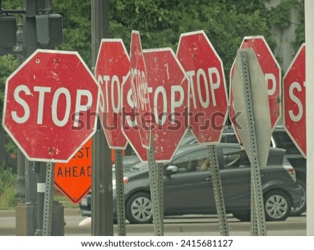 A variety of red stop signs and road signs are positioned near a street with passing cars in the background