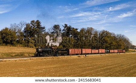 An Aerial View of an Antique Steam Freight Passenger Train Blowing Smoke and Steam, as it Slowly Travels Thru Farmlands on an Autumn Day Royalty-Free Stock Photo #2415683041