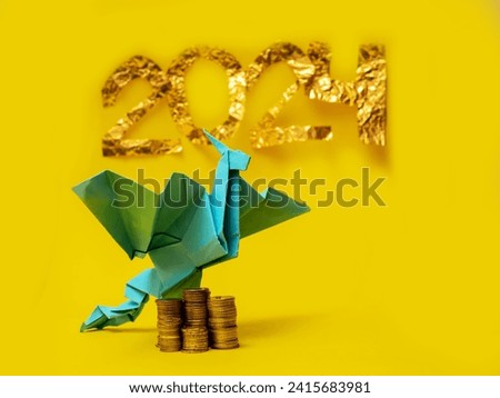 Blue hand made paper dragon over stack of golden coins and sign 2024 on yellow background. Business and finance industry. Horoscope and fortune telling concept.