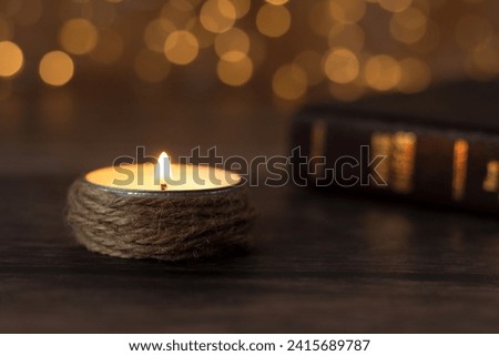 Candle burning with bright flame and closed holy bible book on wooden table with bokeh background. Close-up. Selective focus. Spiritual light shining in the darkness, Christian biblical concept.