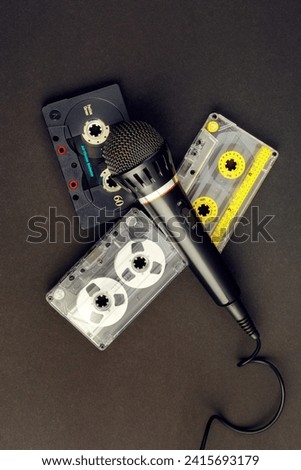 Black professional karaoke microphone and three colorful vintage audio cassettes on a black background. Vertical photo of old 80's analog audio equipment. Royalty-Free Stock Photo #2415693179