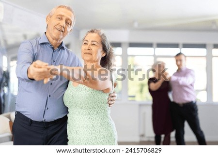 Positive aged woman and man practicing bachata dance moves in pair during group celebration in modern dancing studio Royalty-Free Stock Photo #2415706829